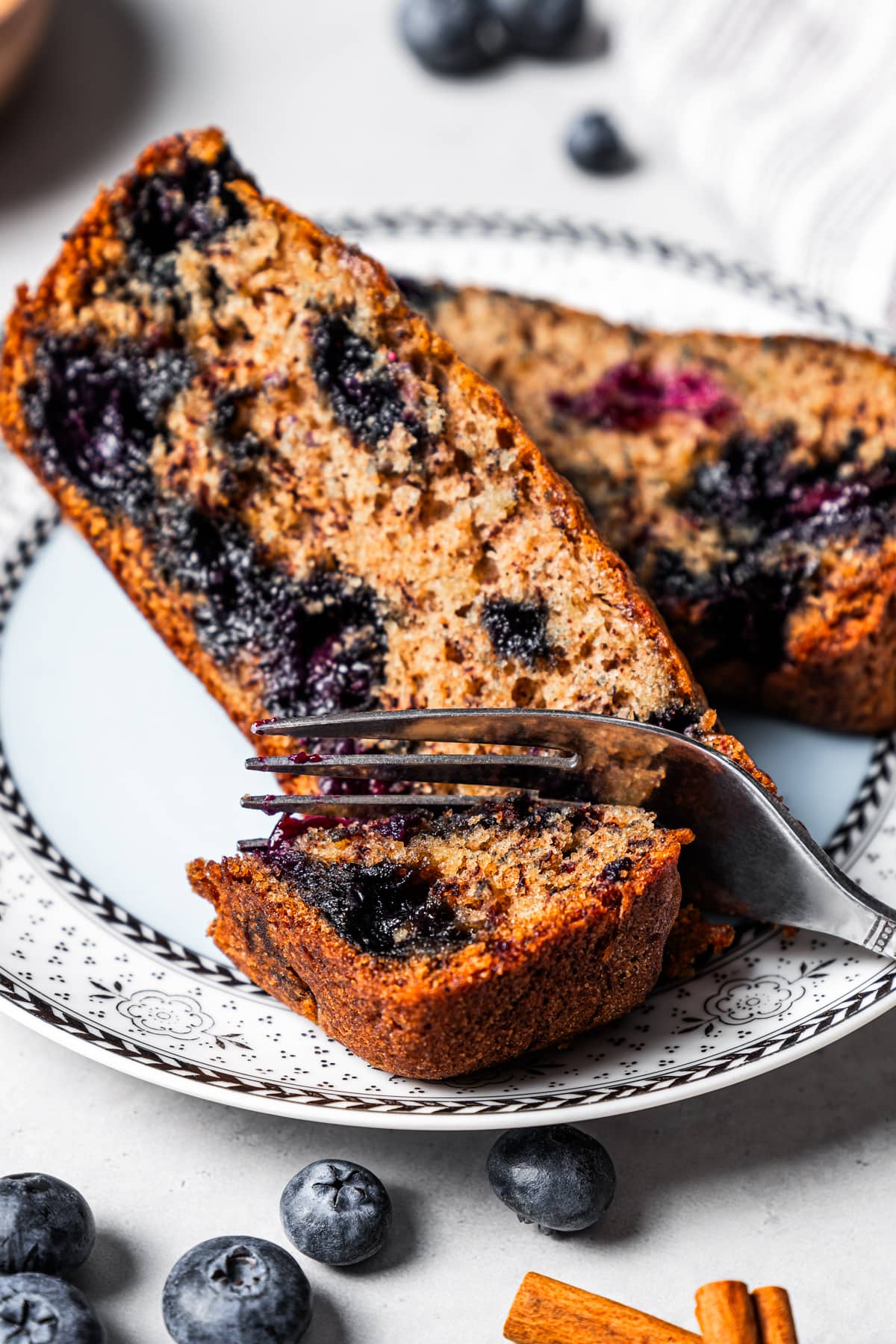 A fork cutting into a slice of blueberry banana bread on a plate.