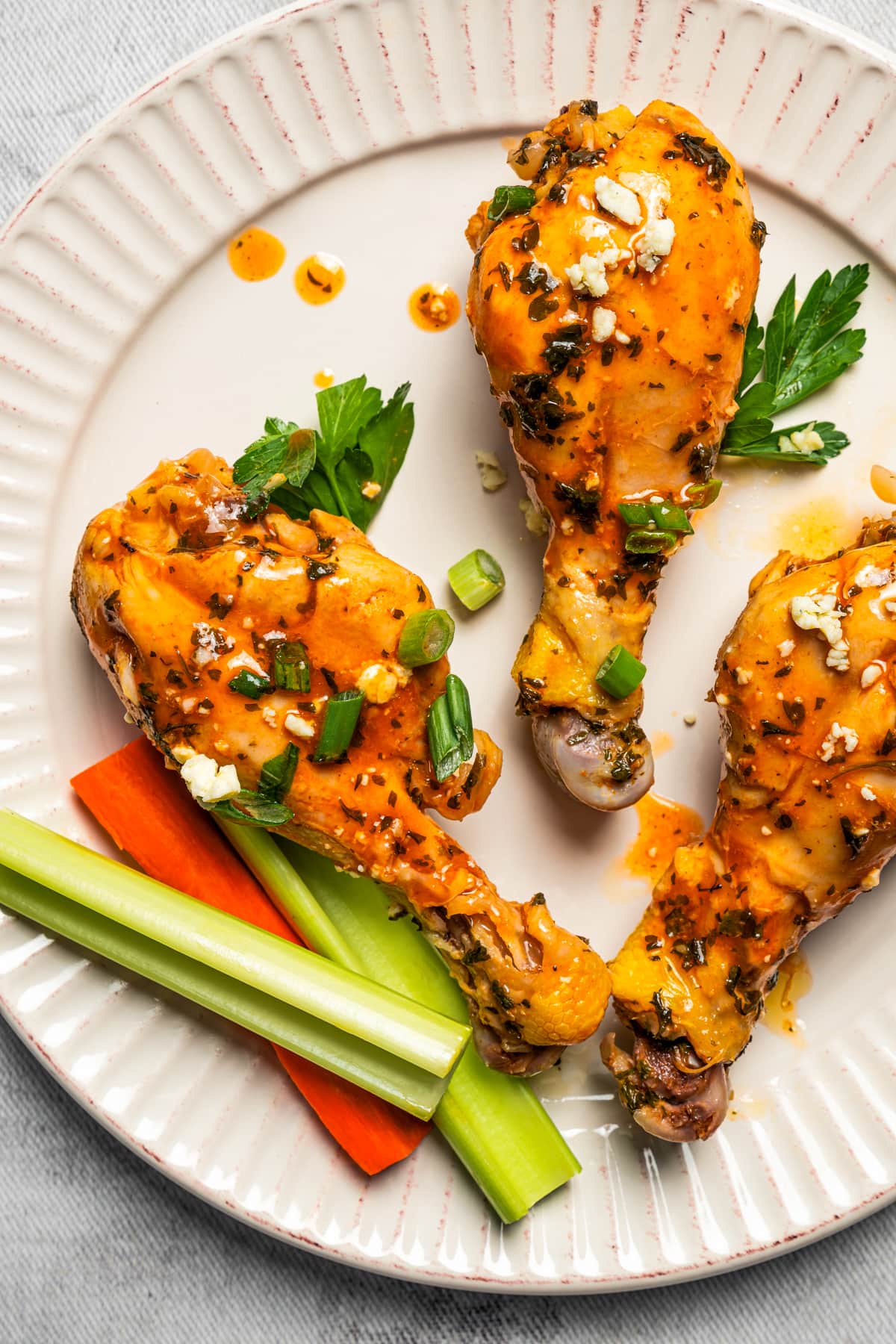 Closeup of buffalo chicken drumsticks topped with buffalo sauce and served on a plate with celery and carrots.