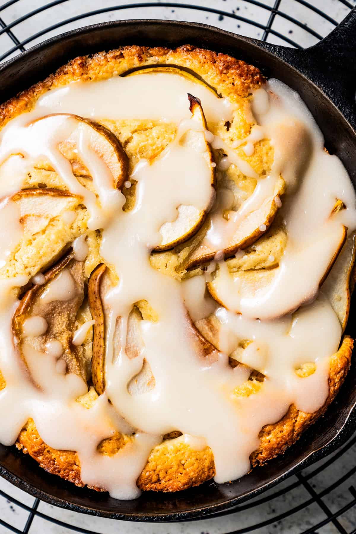 Close up of pear cake in a skillet, with a wire rack underneath.