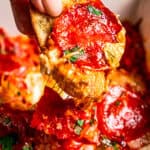 Close up of a hand holding up a slice of bread dipped in cheesy pepperoni pizza dip.