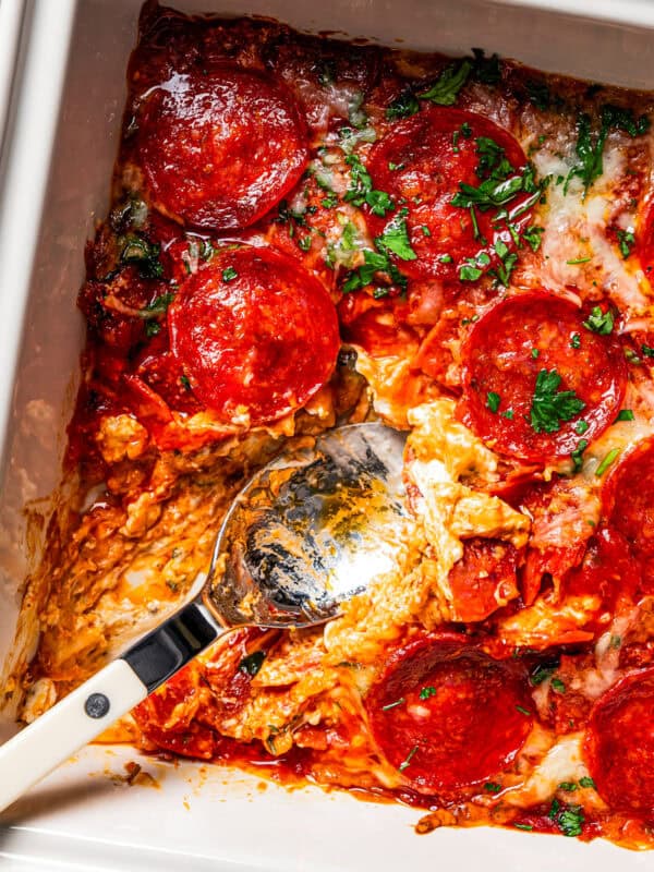 Pepperoni pizza dip in a baking dish with pepperoni on top and a spoon for serving.