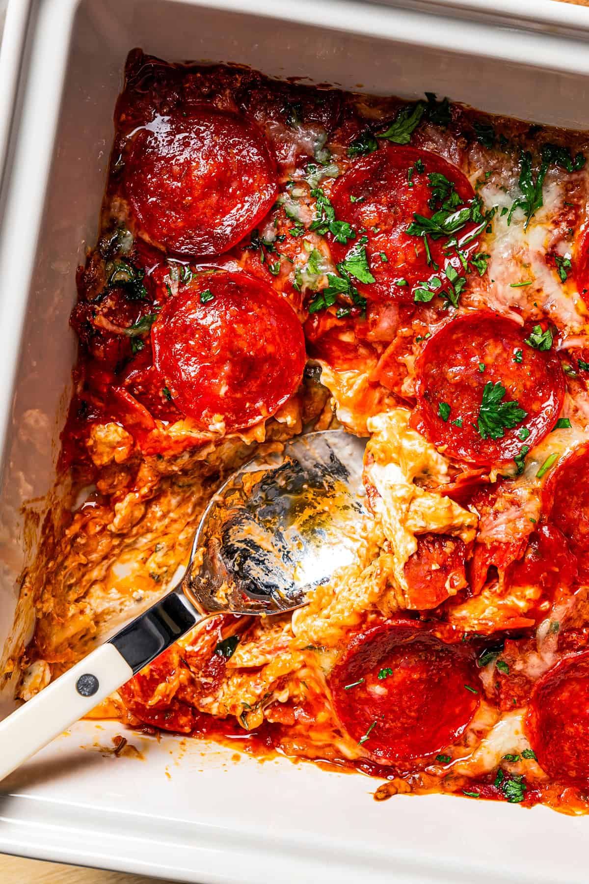 Cheese dip in a baking dish with pepperoni on top and a spoon for serving.