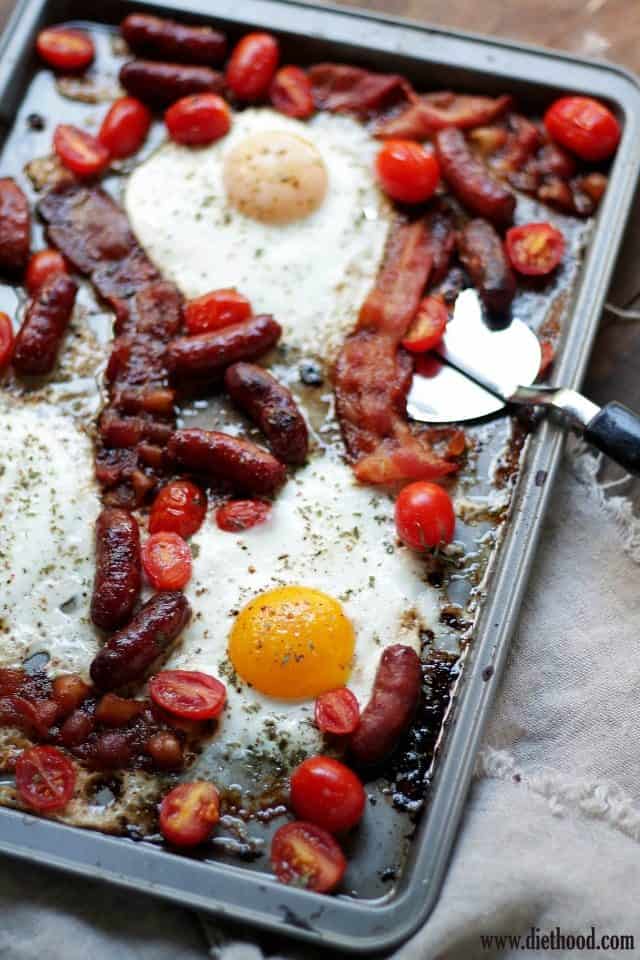 Browned sausages, crispy bacon, eggs, and tomatoes in the baking sheet. 