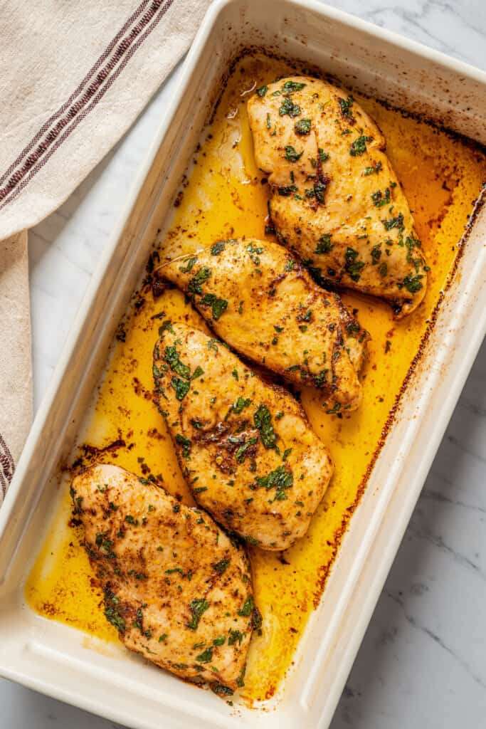 Four seasoned and cooked chicken breasts in a rectangular baking dish
