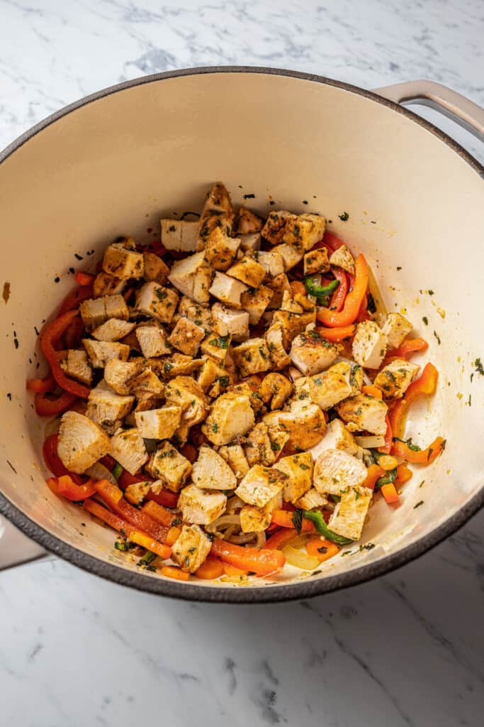 A pot with cubes of chicken on top of onions and bell peppers