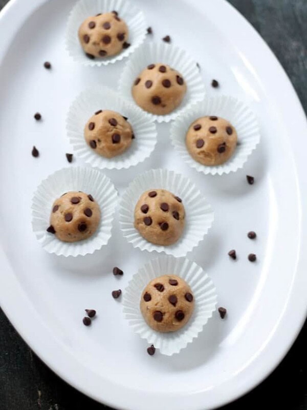 Cookie dough balls are topped with mini chocolate chips and served on a white platter.