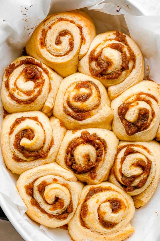 Pumpkin pie cinnamon rolls arranged in a baking pan lined with parchment paper.