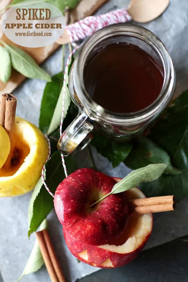 Spiked Apple Cider in a glass mug next to apples with cinnamon sticks