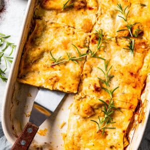 Overhead view of butternut squash lasagna cut into slices in a baking dish, with a spatula resting in an open space.