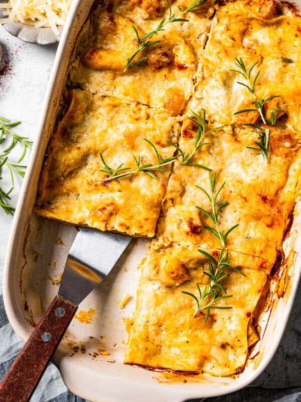 Overhead view of butternut squash lasagna cut into slices in a baking dish, with a spatula resting in an open space.