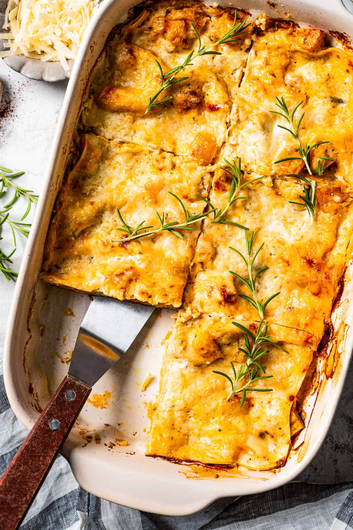 Overhead view of butternut squash lasagna cut into slices in a baking dish, with a spatula resting in an open space.