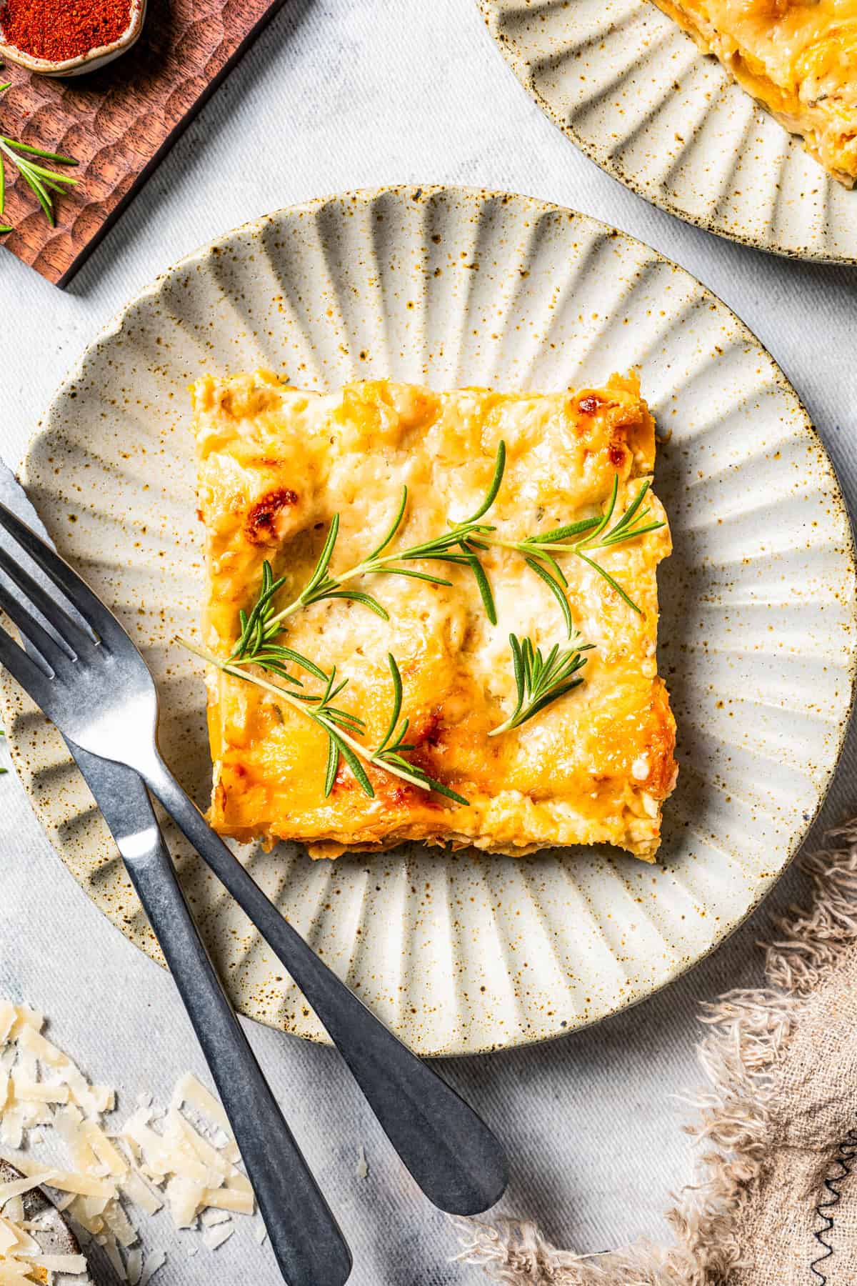 Overhead view of a slice of butternut squash lasagna on a white plate next to a fork and knife.