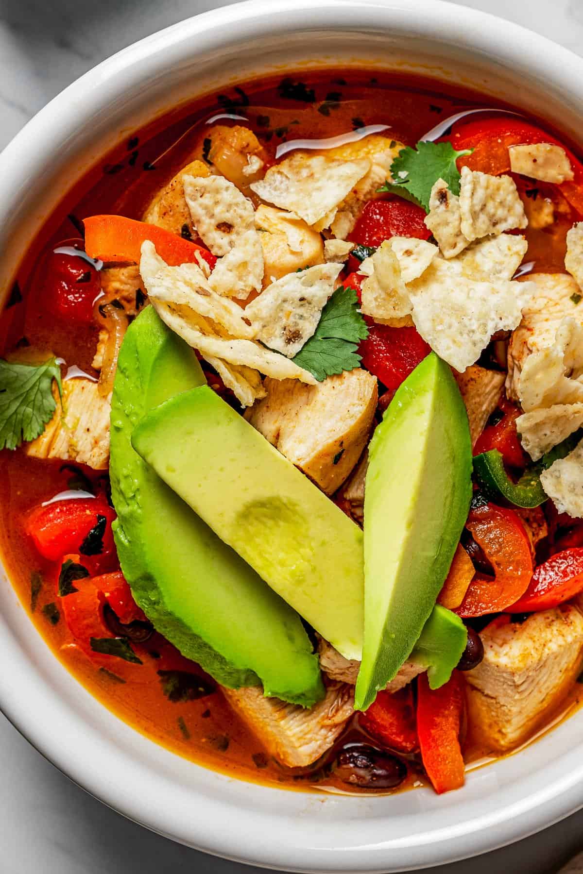 Close-up overhead view of a bowl of tortilla soup topped with crumbled tortilla chips and avocado.