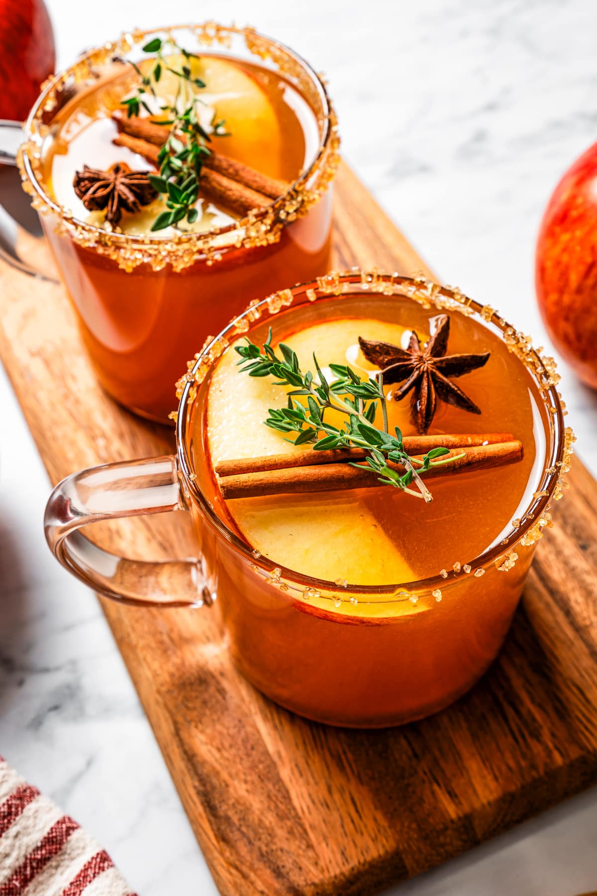 Two mugs of spiked apple cider garnished with cinnamon sticks, star anise, and apple slices.