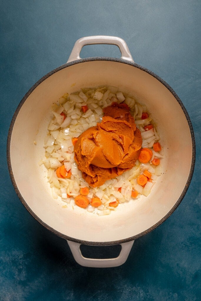 Pumpkin puree added to a large pot with diced onions and carrots.
