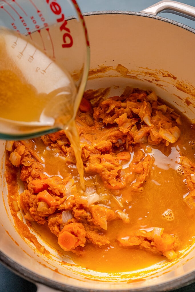 Chicken stock is poured into a pot with pumpkin puree and diced carrots and onions.