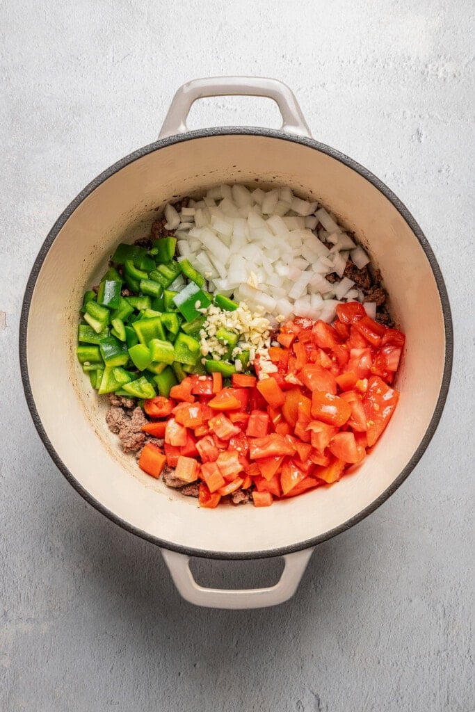 Diced tomatoes, onions, and green bell peppers added to a pot with ground beef.