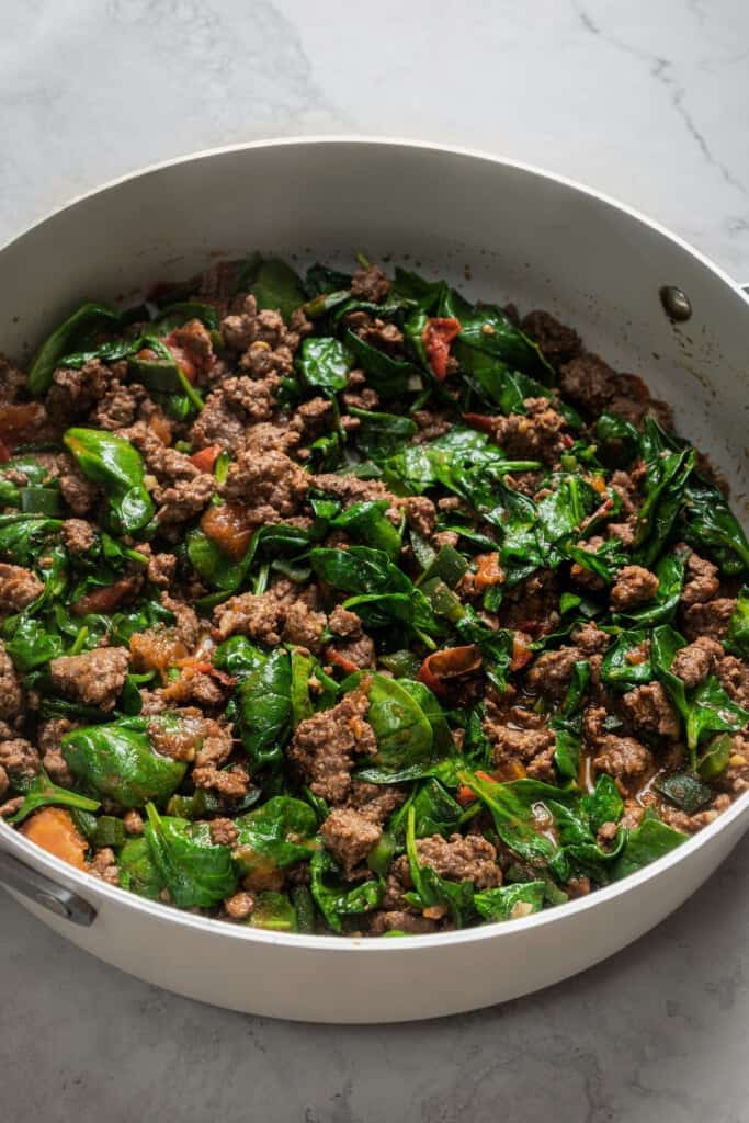 Wilted spinach added to a skillet with ground beef taco meat.