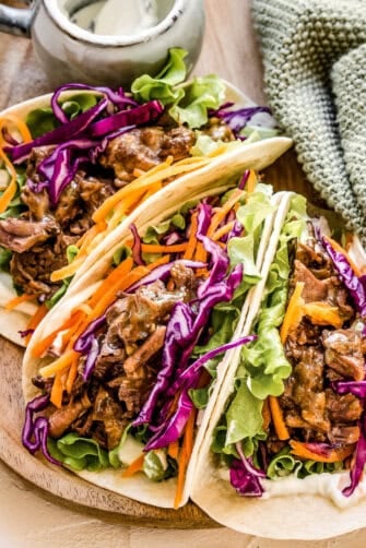 Three Korean beef tacos filled with shredded BBQ beef and veggies, served on a plate.