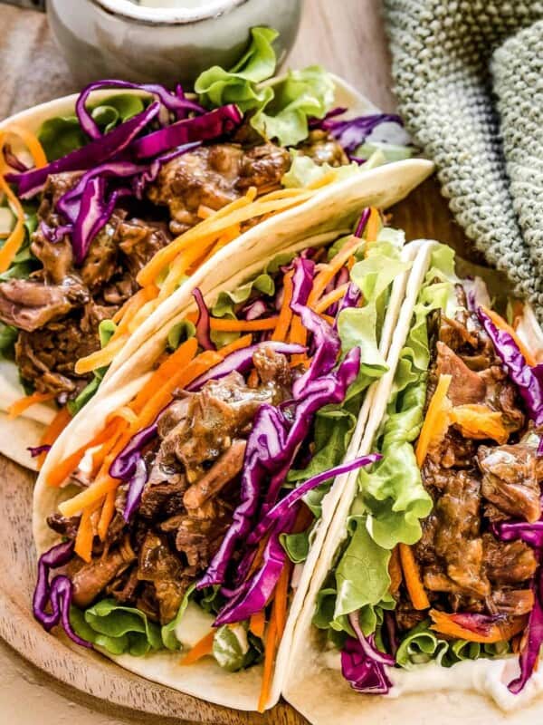 Three Korean beef tacos filled with shredded BBQ beef and veggies, served on a plate.
