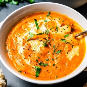 A bowl of pumpkin soup topped with a drizzle of cream and fresh herbs and set next to a second bowl in the background.