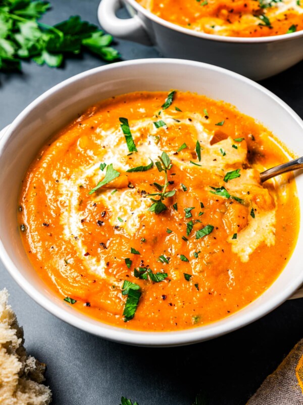 A bowl of pumpkin soup topped with a drizzle of cream and fresh herbs and set next to a second bowl in the background.