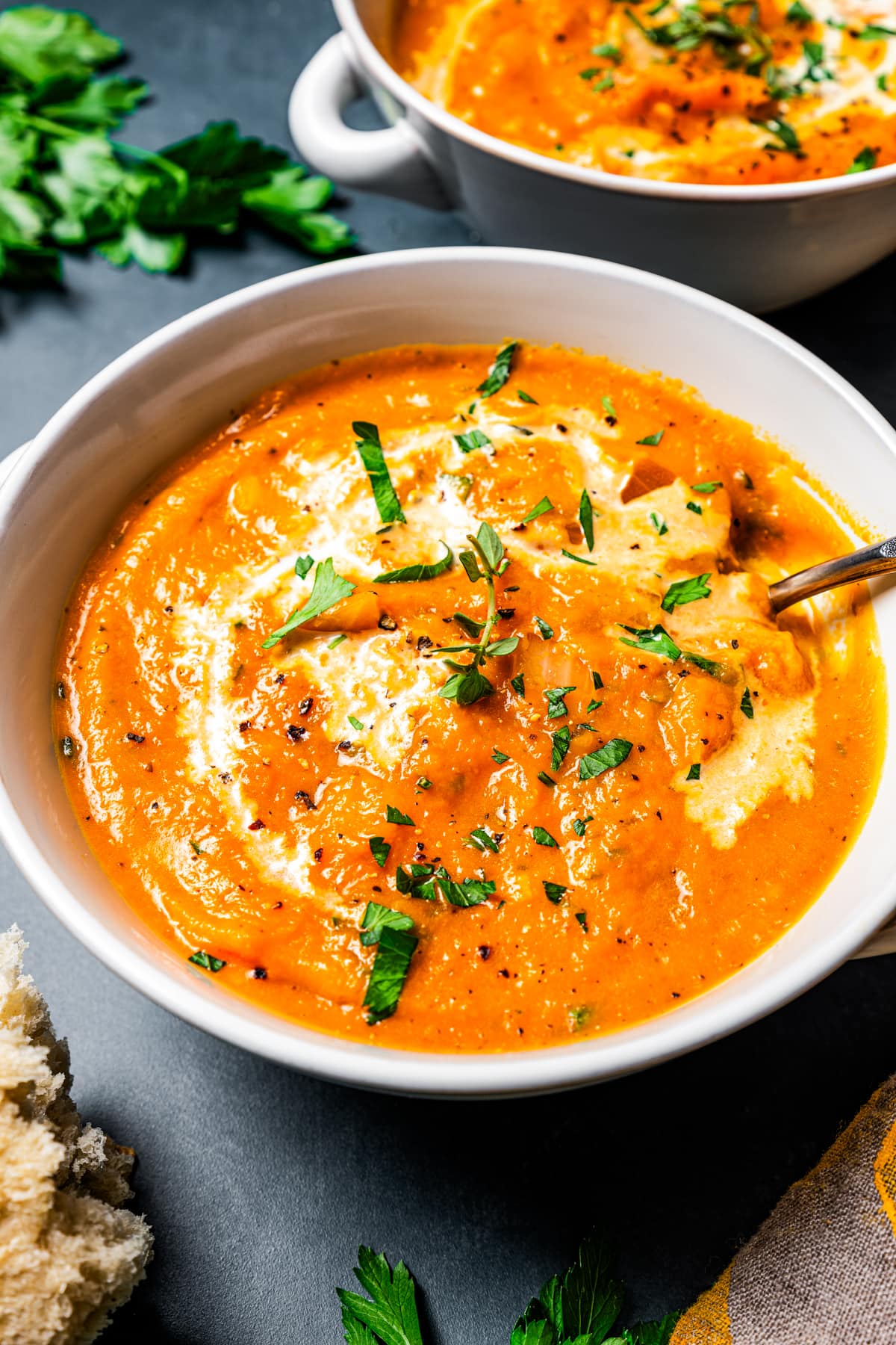 A bowl of pumpkin soup topped with a drizzle of cream and fresh herbs and set next to a second bowl in the background.