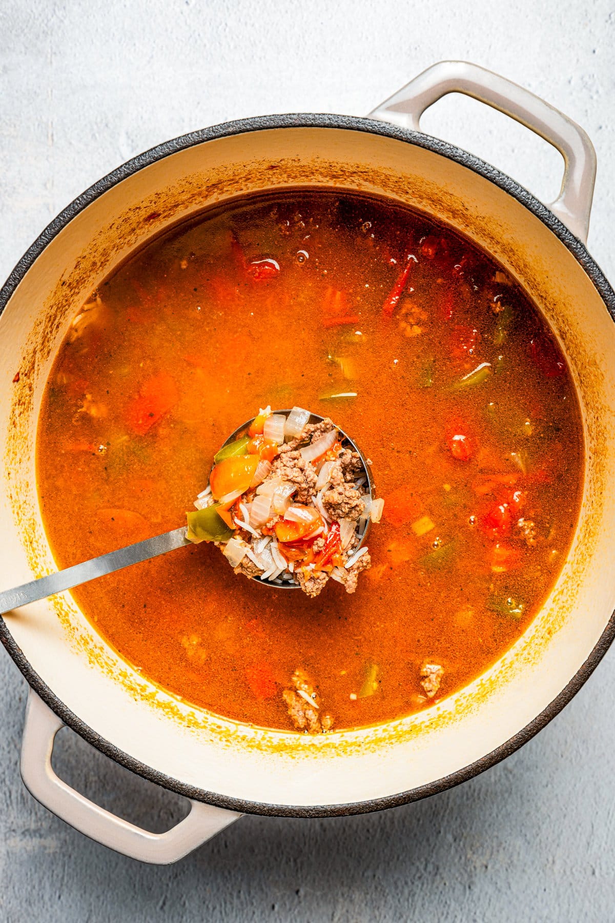 Dutch oven filled with soup and a ladle spooning out a portion of it.