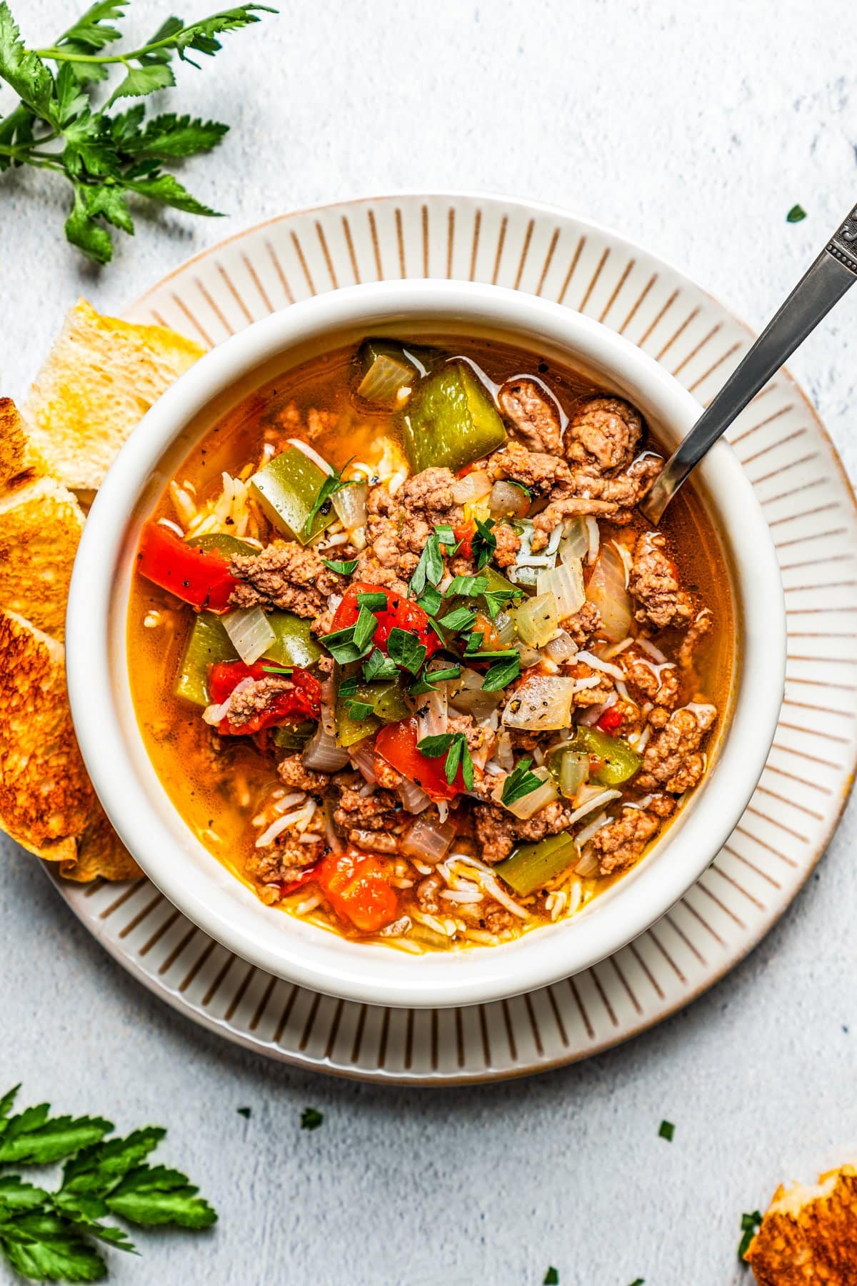 Overhead image of a soup bowl filled with stuffed pepper soup and set on a dinner plate with slices of bread set next to the bowl.