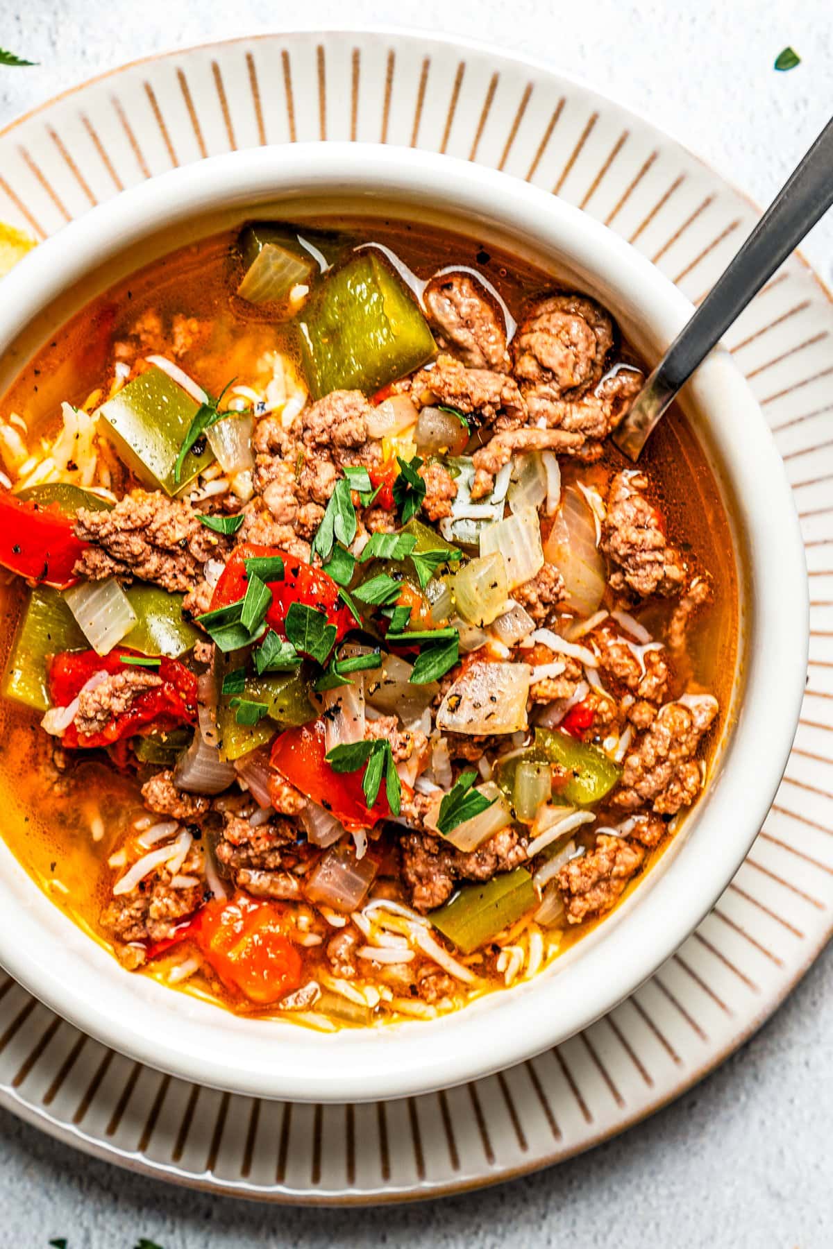 Overhead close-up image of a soup bowl filled with stuffed pepper soup and set on a dinner plate.