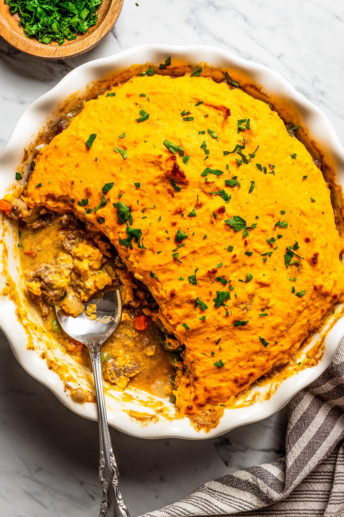 Overhead view of a baking dish with a sweet potato shepherd's pie and a spoon resting inside of the baking dish.