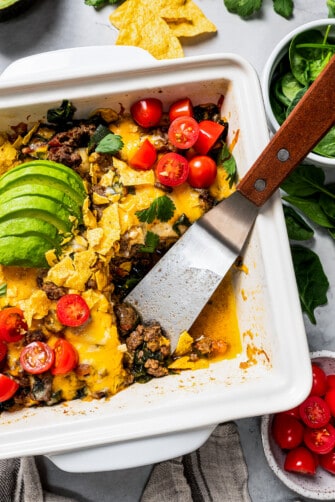Overhead view of a baked taco casserole in a square baking dish with a serving missing from the corner, with a spatula left in the pan.