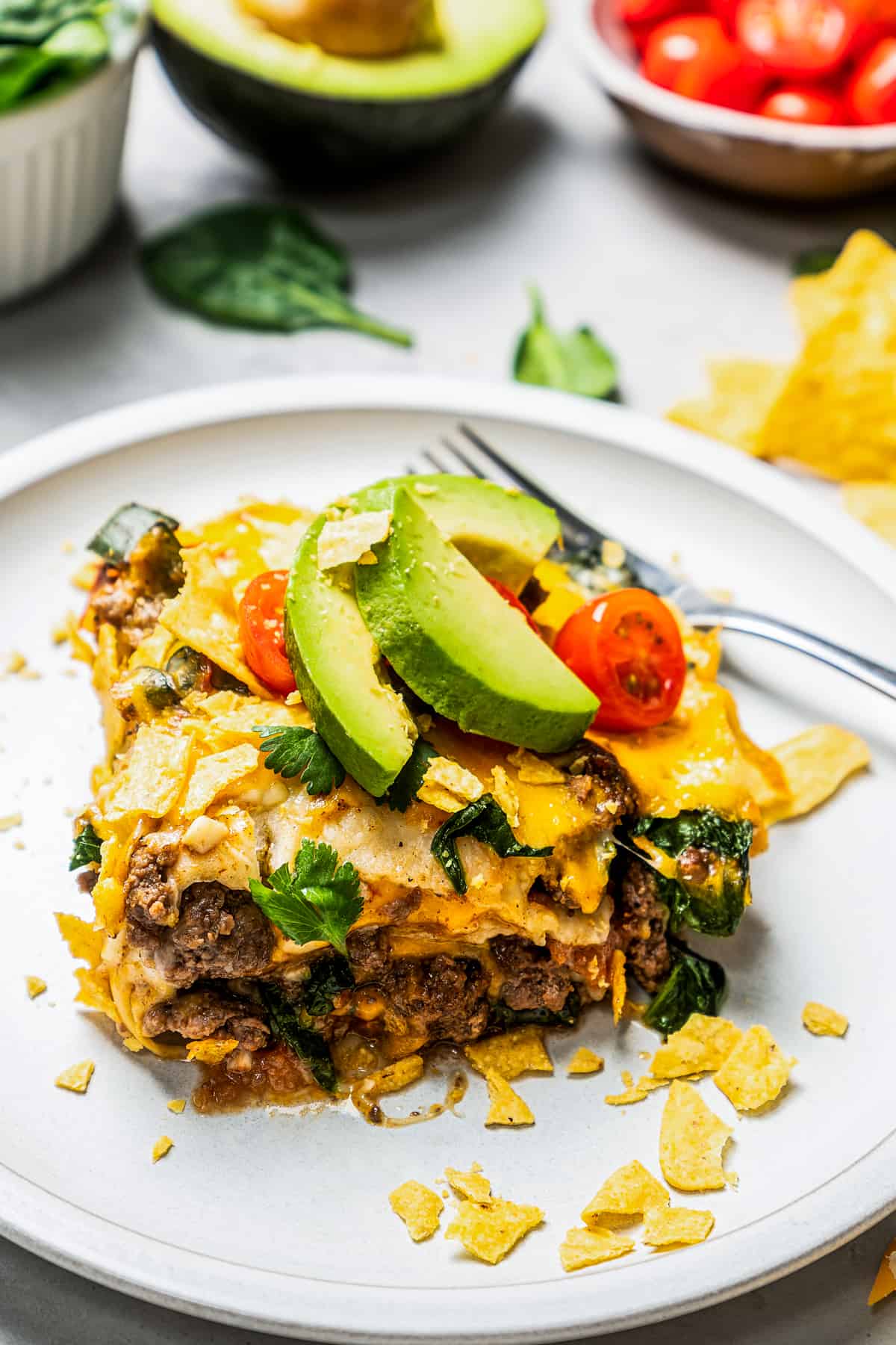 A serving of taco casserole on a white plate garnished with avocado slices and cherry tomatoes.