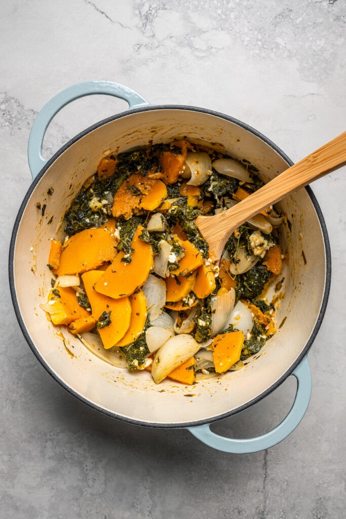 Canned spinach stirred into butternut squash and onions in a large pot.