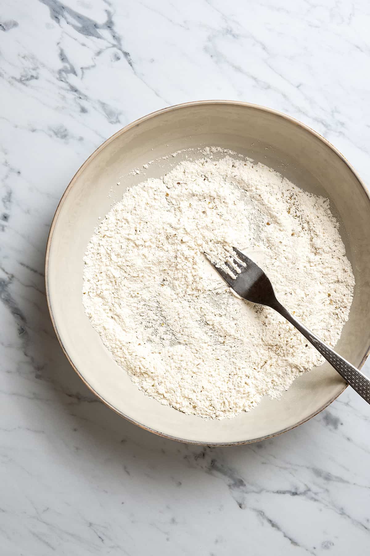 Flour and seasonings combined with a fork in a mixing bowl.
