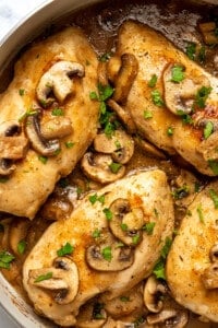 Close up top view of chicken marsala in a large skillet, topped with mushrooms and marsala wine sauce.