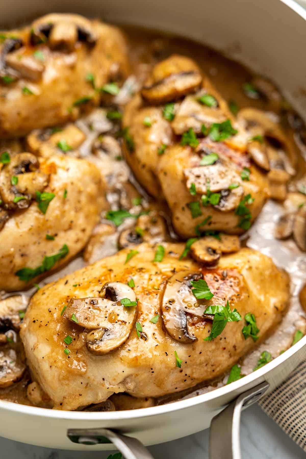 Close up of chicken marsala in a large skillet, topped with mushrooms and marsala wine sauce.