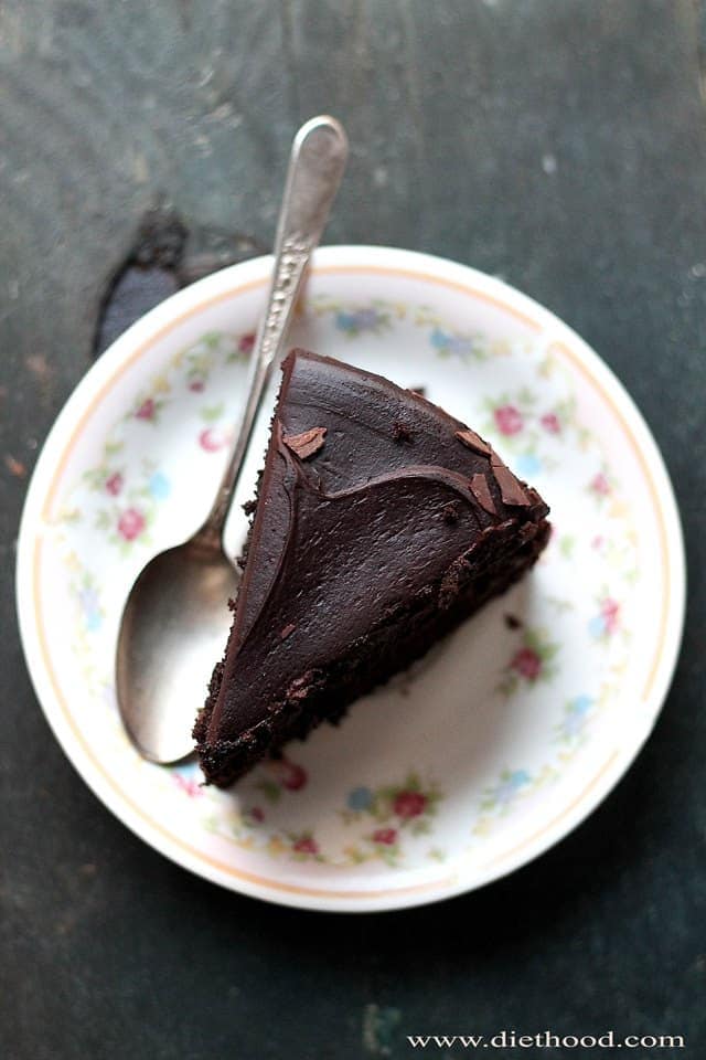 A slice of black magic chocolate cake served on a plate with a spoon set next to it.