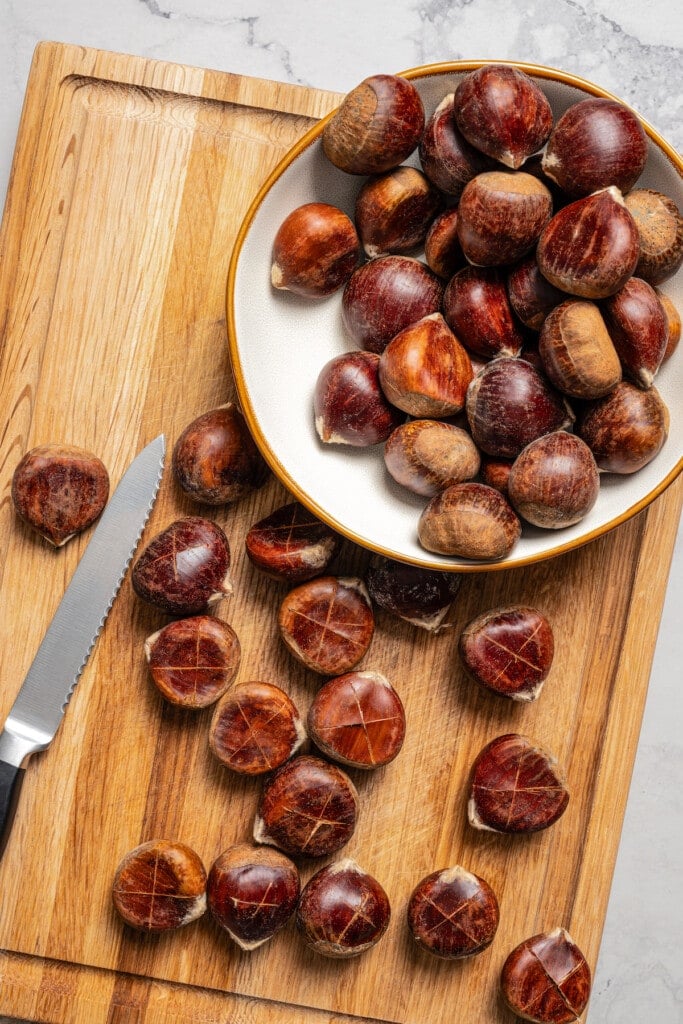 Fresh chestnuts in a bowl on a cutting board.