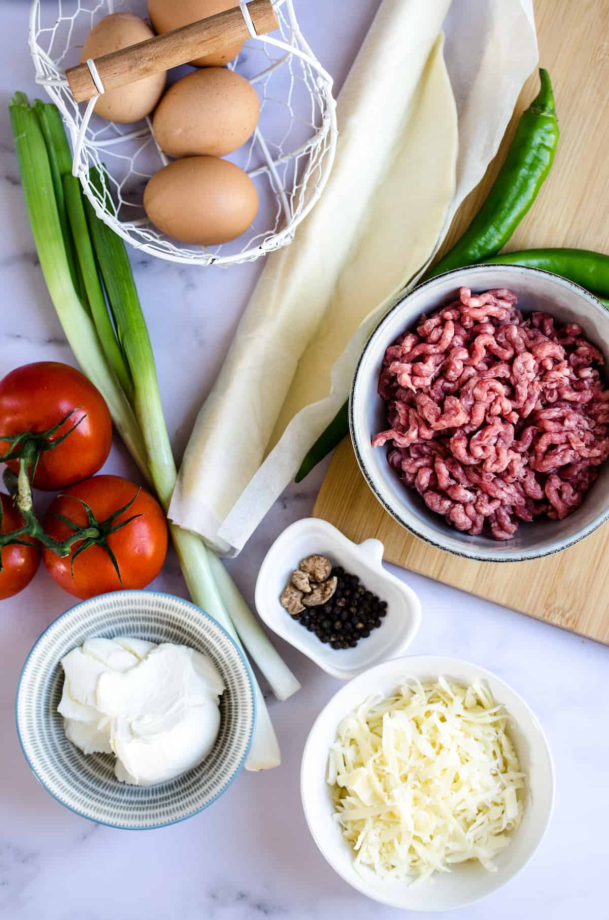 The ingredients for easy Tex-Mex Quiche: eggs, ground beef, tomatoes, green onions, whipped cream cheese, seasoning, green chilies, and shredded cheese.