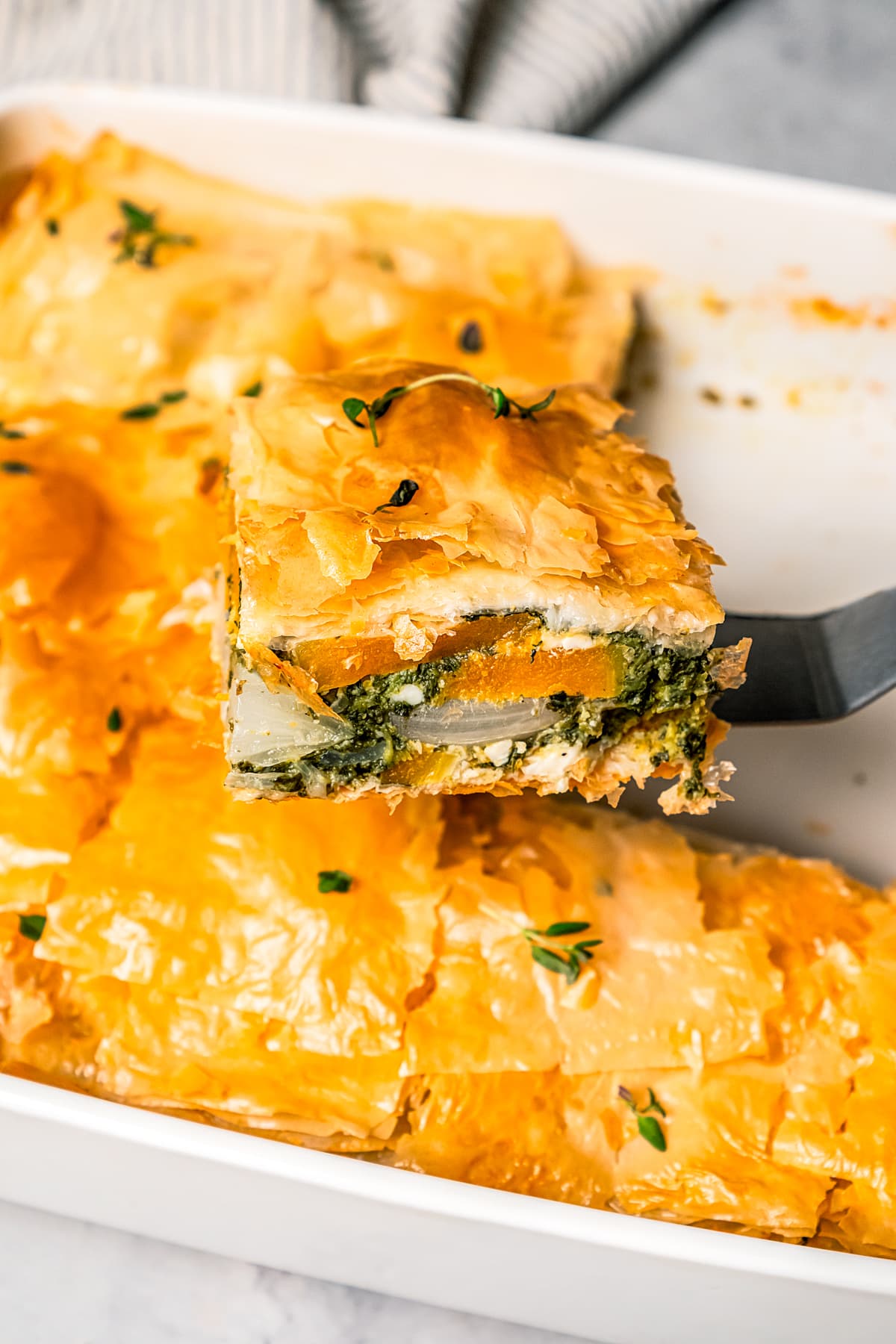 A slice of butternut squash and spinach pie lifted from a baking dish.