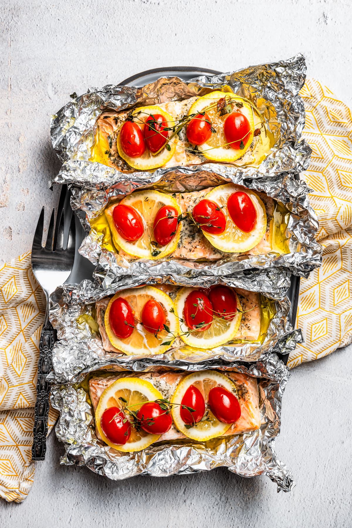 Overhead view of baked lemon pepper salmon filets topped with lemon slices, tomatoes, and thyme inside unwrapped foil packets.