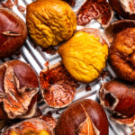 Close-up photo of roasted chestnuts, some outside of the shell and some are inside of their shells.