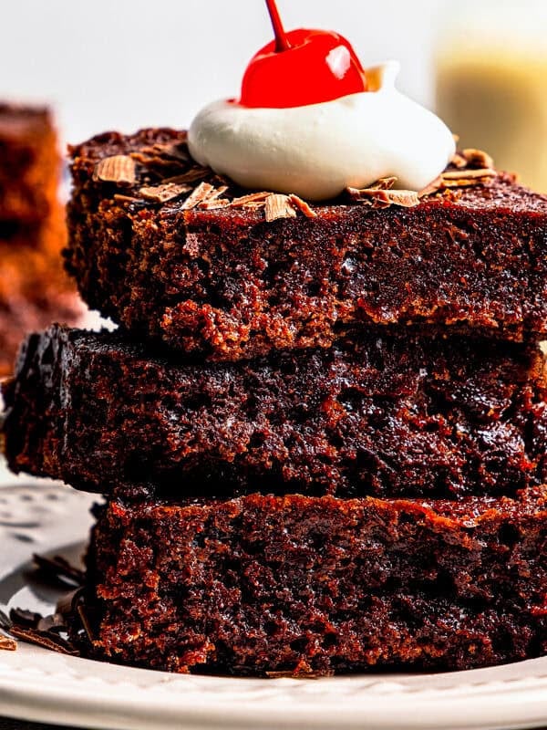 A stack of three brownies topped with a dollop of whipped cream and a maraschino cherry.