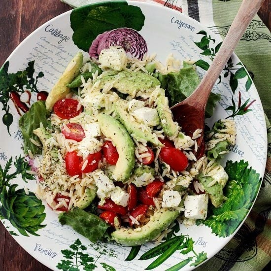 Avocado and Feta Cheese Orzo Salad on a decorative plate with a wooden spoon