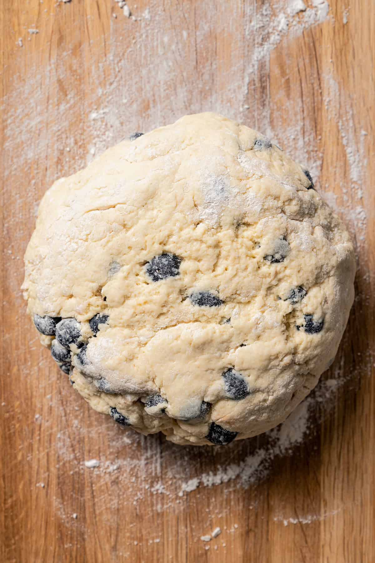 A large ball of blueberry scone dough on a floured wooden surface.
