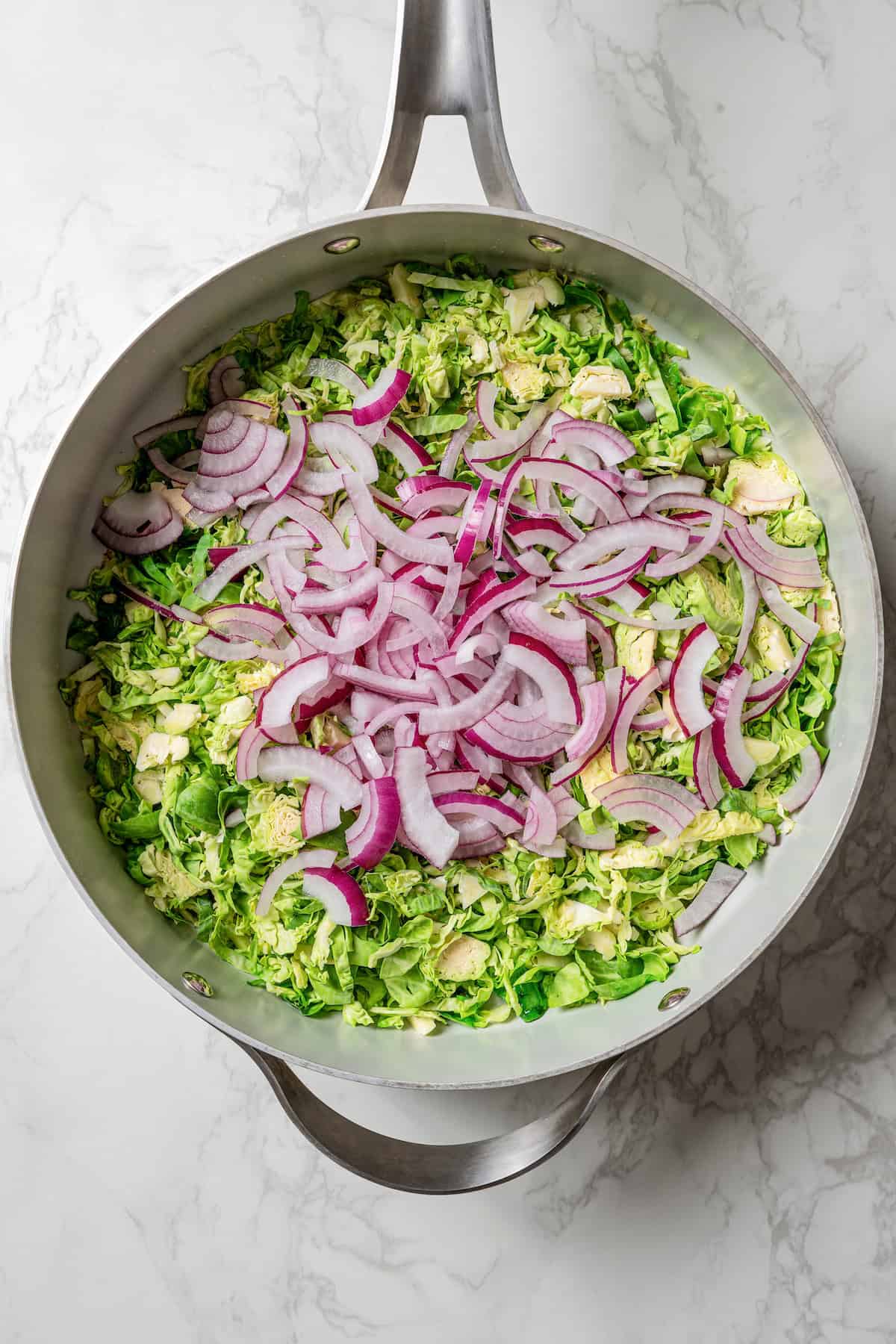 Sliced red onion added to shaved Brussel sprouts in a skillet.