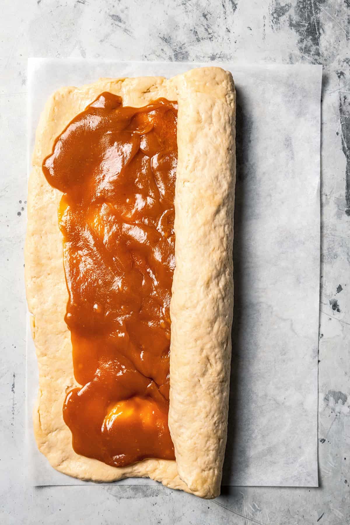 These sweet and gooey homemade caramel rolls require no yeast, rise time, or kneading. They're easy, quick, and best of all, delicious! Dough being rolled up around caramel filling.