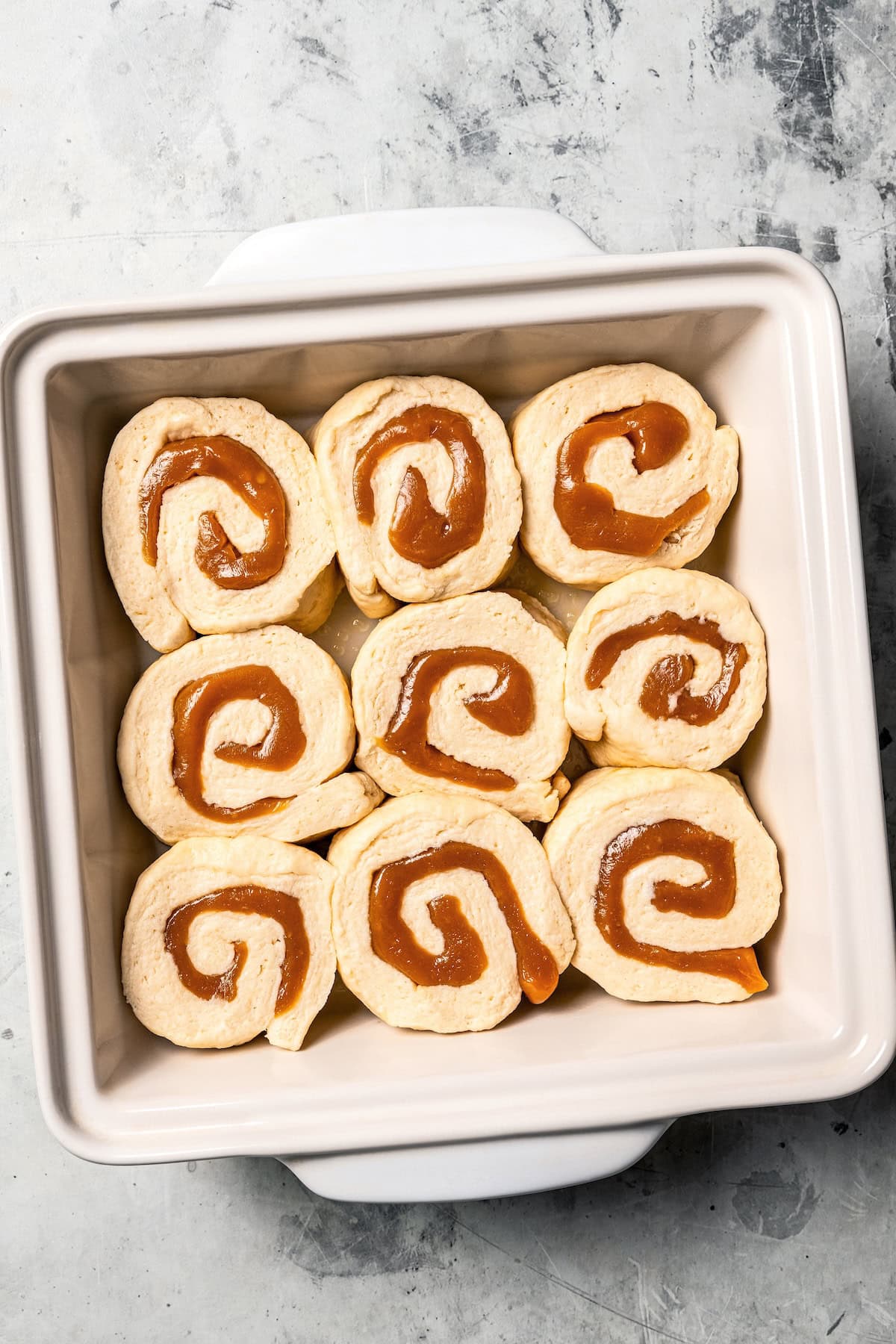 These sweet and gooey homemade caramel rolls require no yeast, rise time, or kneading. They're easy, quick, and best of all, delicious! Overhead view of unbaked caramel rolls in a baking dish.