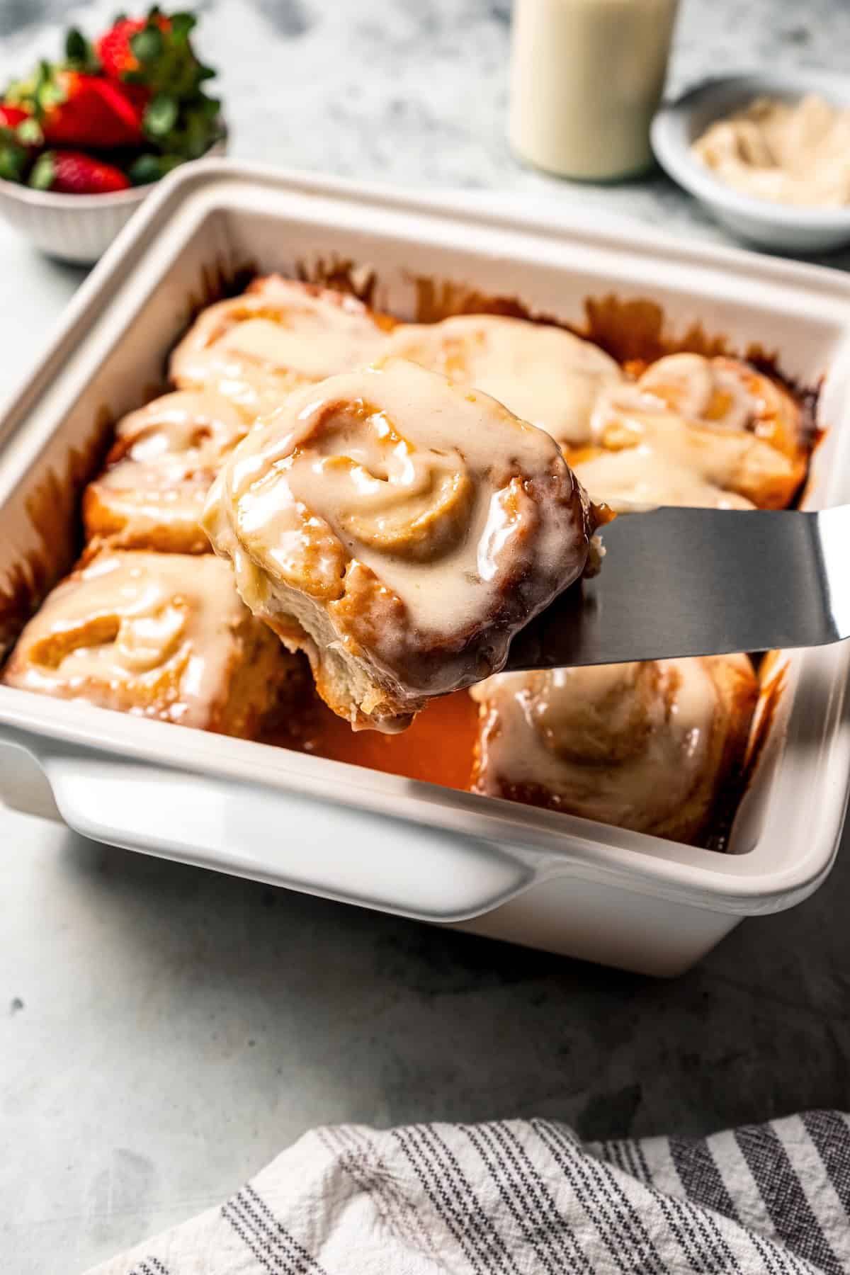 These sweet and gooey homemade caramel rolls require no yeast, rise time, or kneading. They're easy, quick, and best of all, delicious! A spatula lifting a gooey caramel roll from a baking dish of rolls.